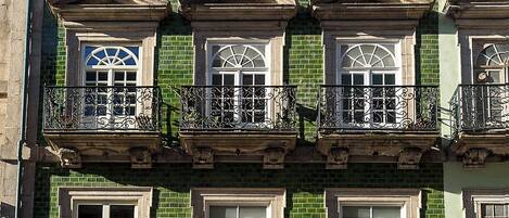 A multi-story building with a green brick facade, multiple windows, and balconies with wrought iron railings.