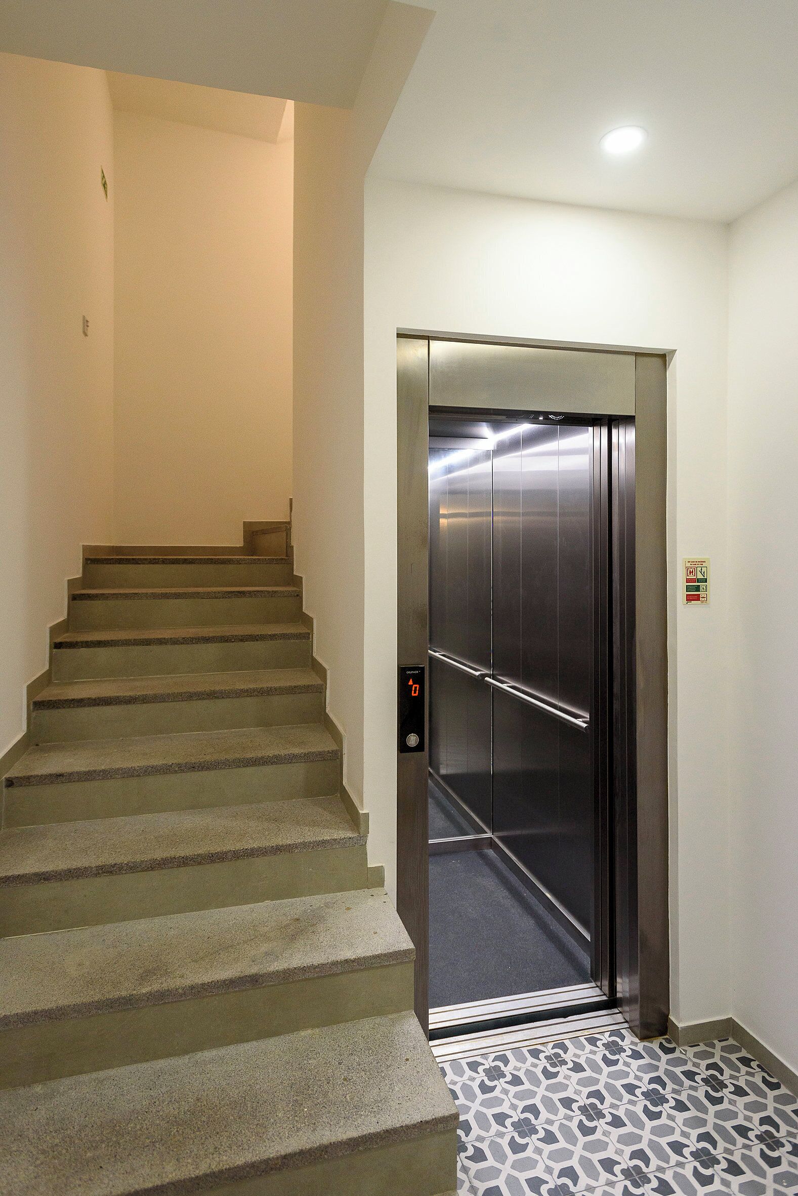 A staircase leading to an elevator with a control panel and a safety sign.