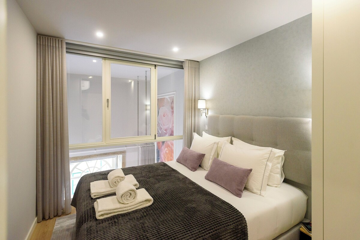 A hotel room with a bed, a window, a nightstand, and a lamp.
