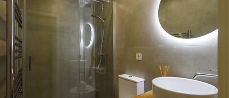 A modern bathroom with a glass-enclosed shower, a toilet, a sink with a round basin, and a mirror with a circular design on the wall.