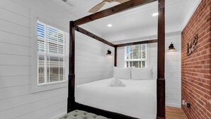 A four-poster bed with white bedding, a bench at the foot, and a brick wall. - Myrtle Beach Family Retreat-Spacious 4BR (Myrtle Beach)
