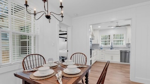 A dining room with a wooden table set for four, white walls, and a view into the kitchen. - Myrtle Beach Family Retreat-Spacious 4BR (Myrtle Beach)