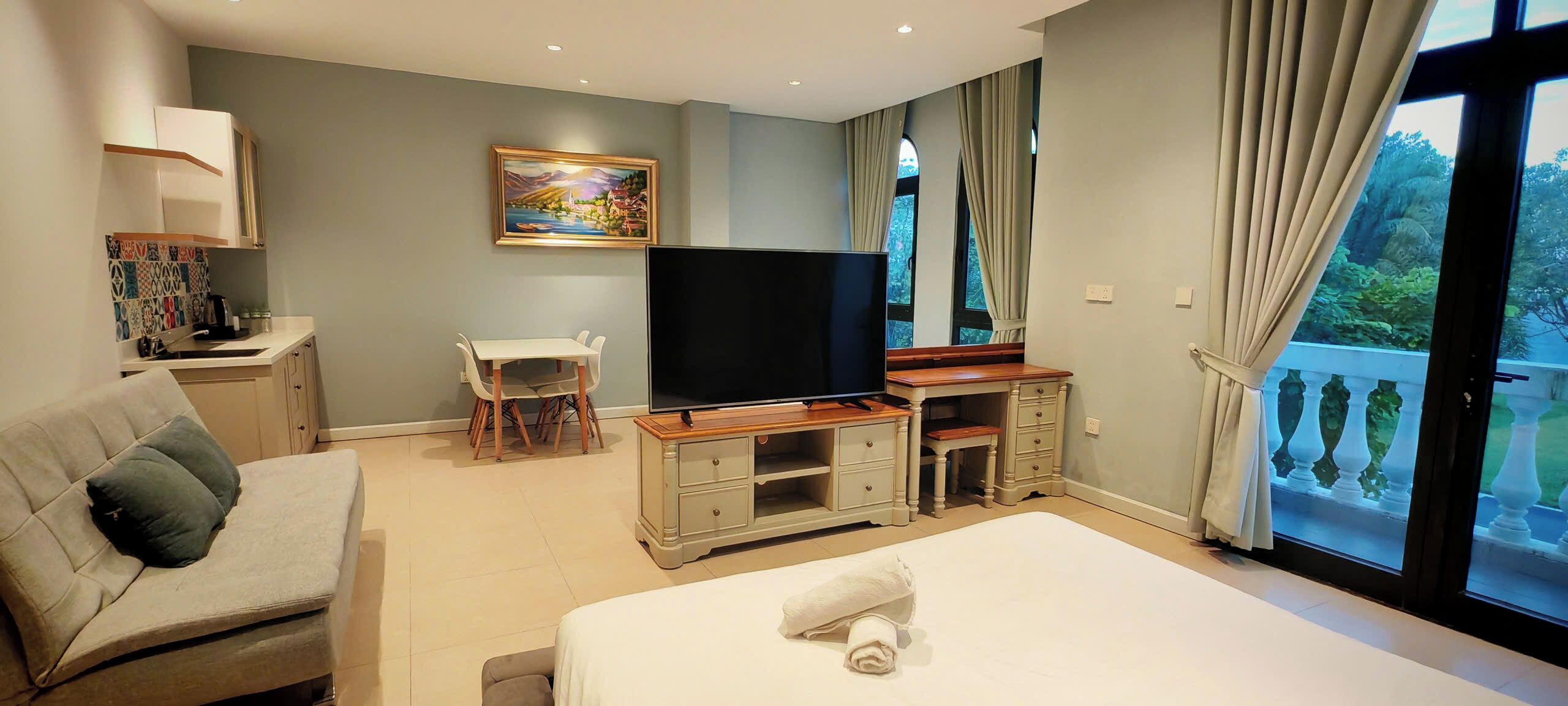 A bedroom with a bed, a TV, a desk, a chair, a sofa, and a balcony with a view.