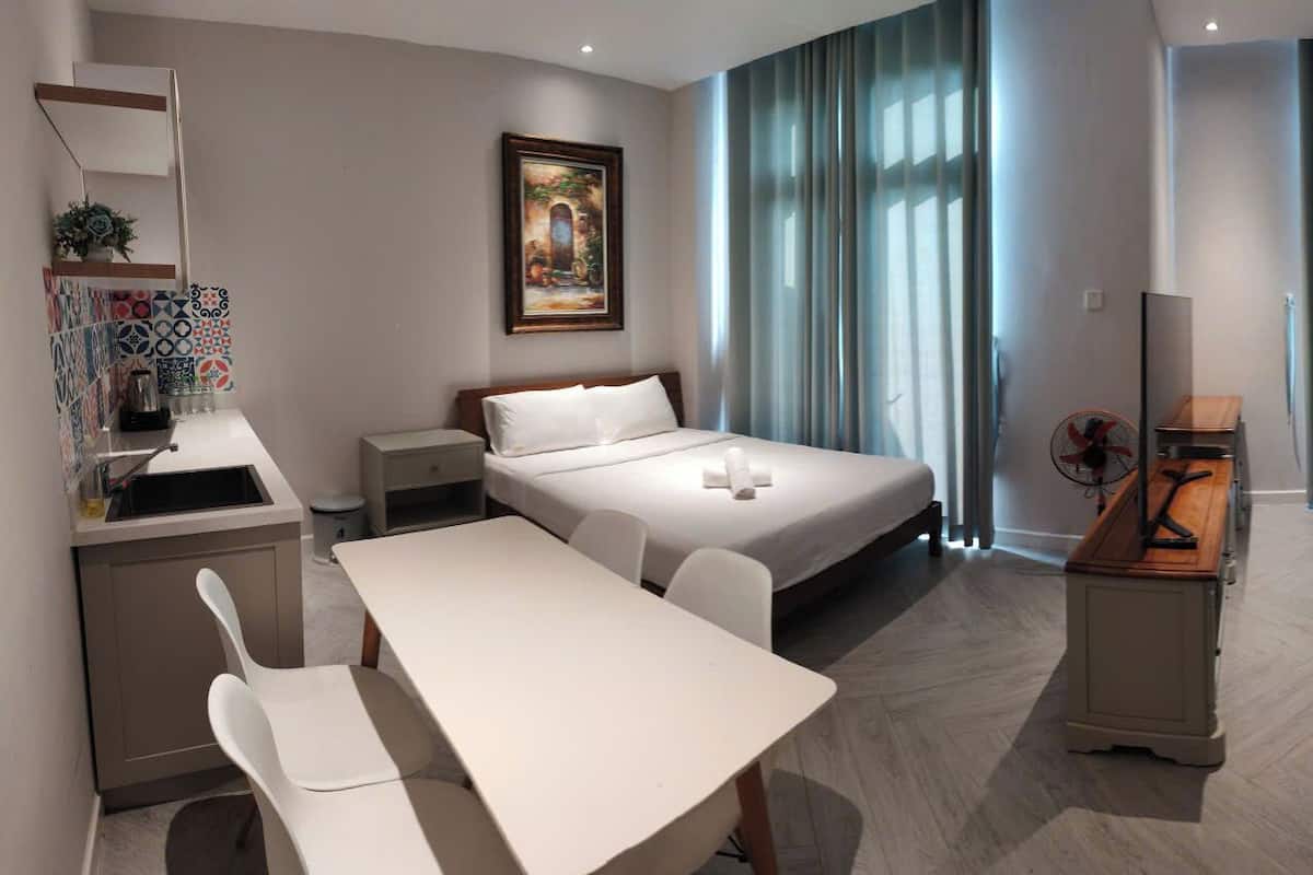 Une chambre d’hôtel avec deux lits, un bureau, une chaise, une petite table, un ventilateur et un tableau au mur.