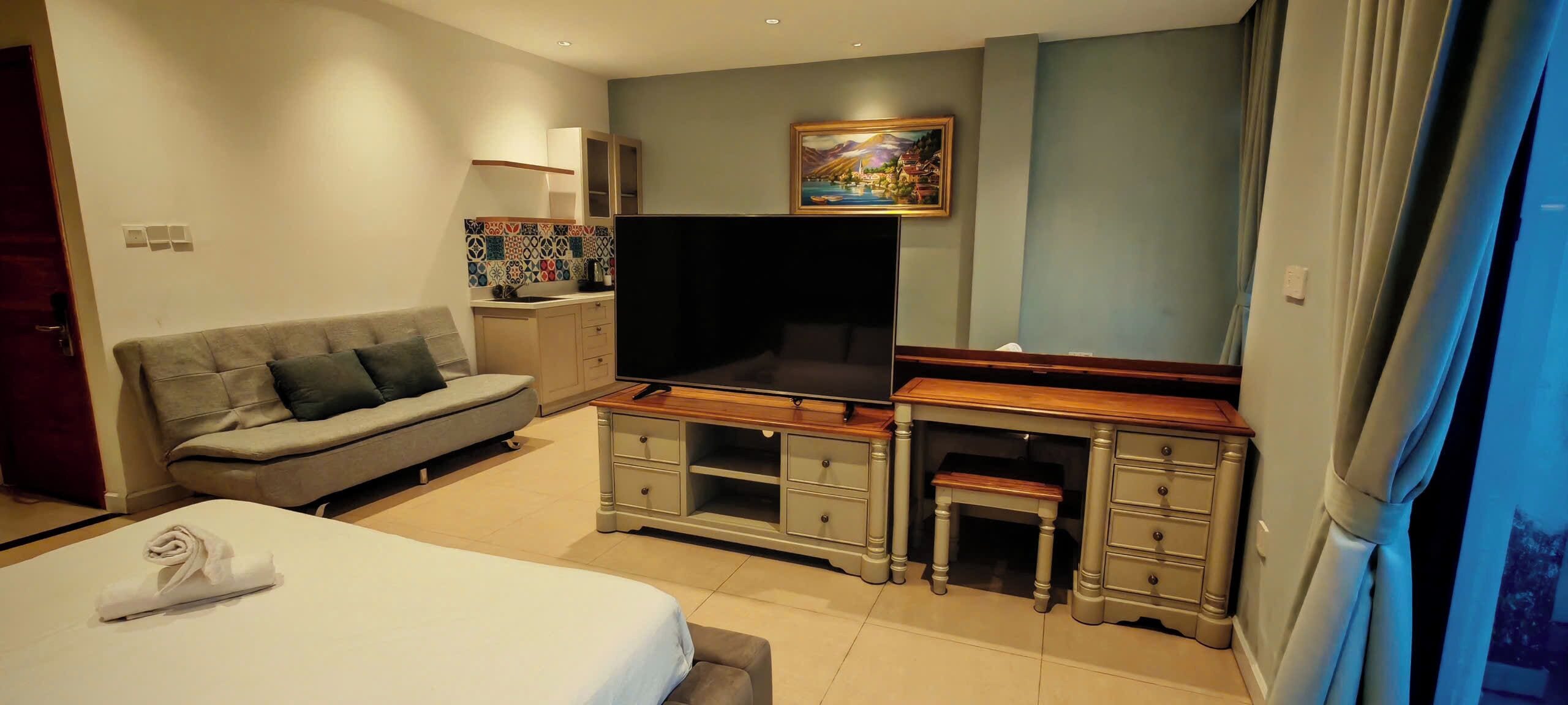 A hotel room with a bed, a sofa, a TV, a desk, and a painting on the wall.