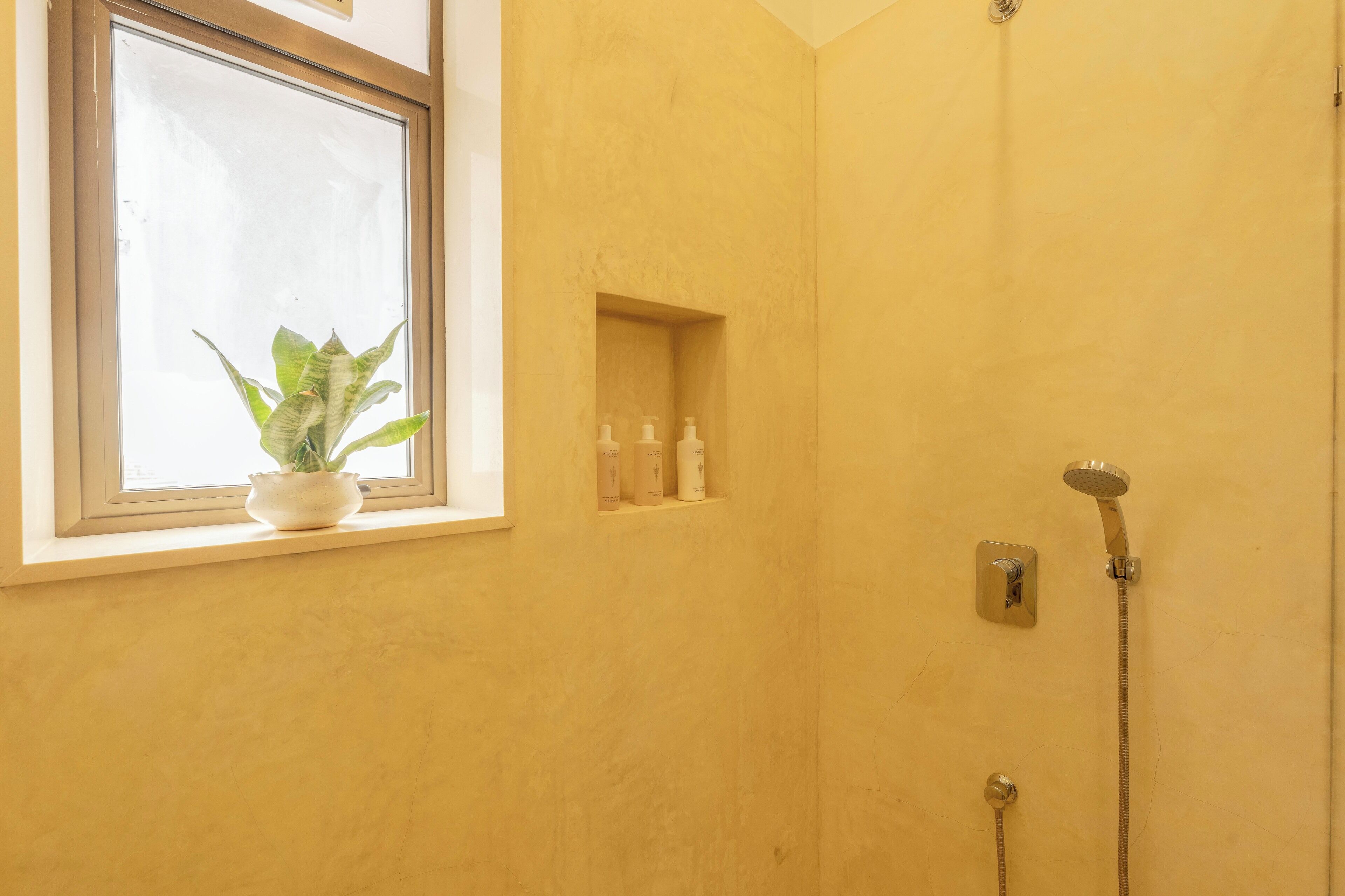 A bathroom with a window, a potted plant, and a shower.