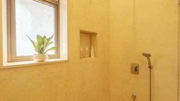A bathroom with a window, a potted plant, and a shower.