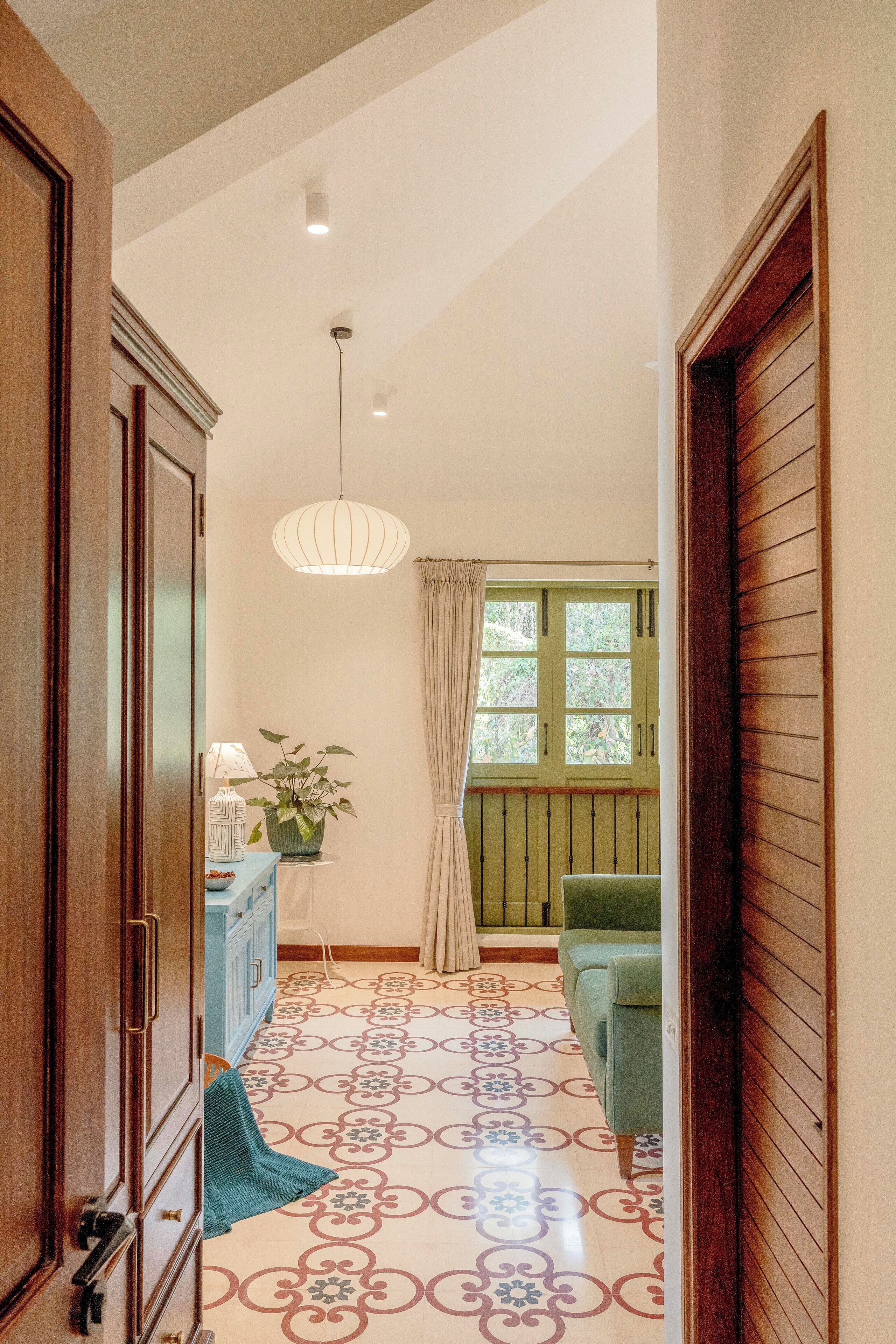 A hallway with patterned flooring, a green sofa, a potted plant, and a hanging light fixture.