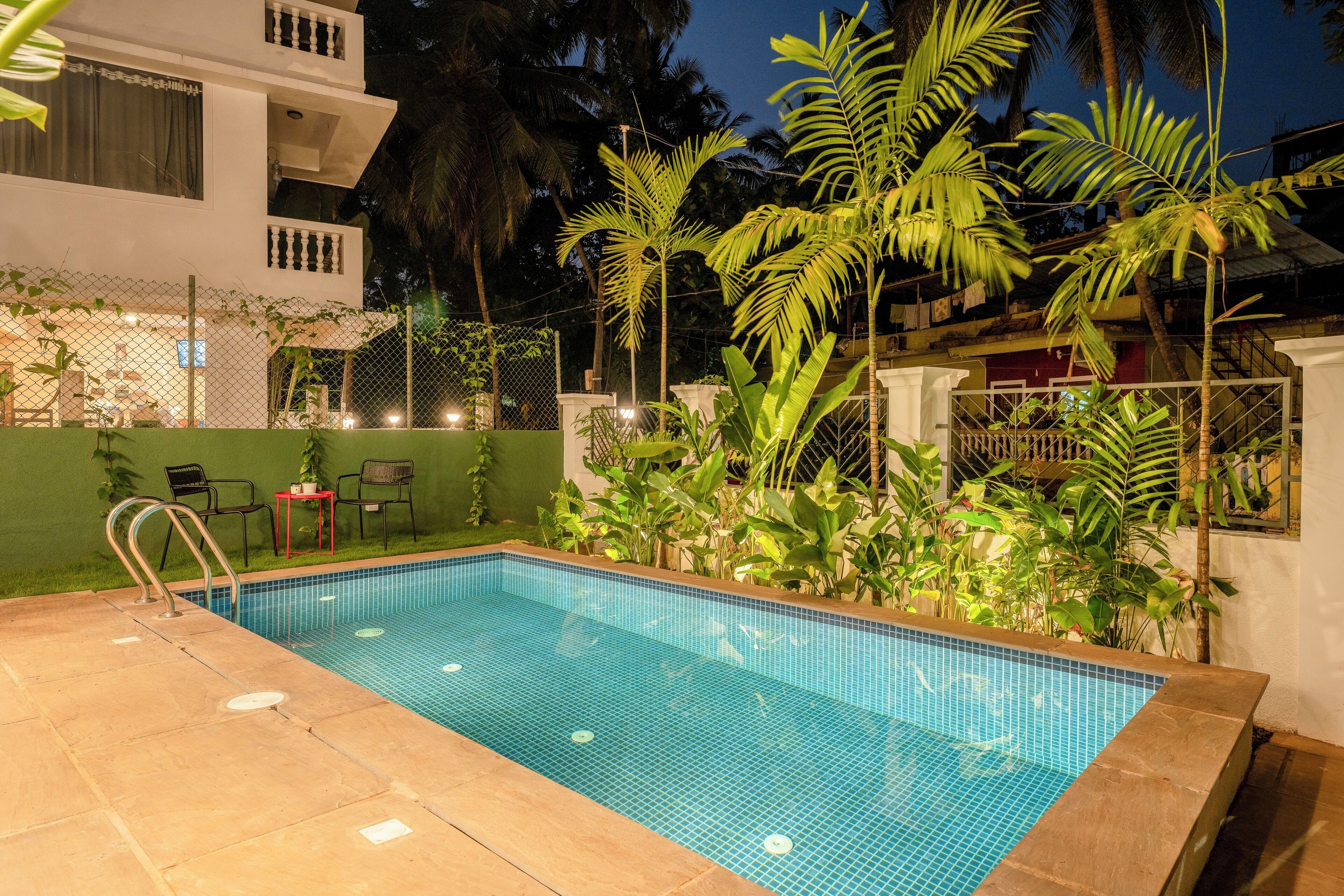 A swimming pool with a tiled edge, surrounded by plants and a fence.