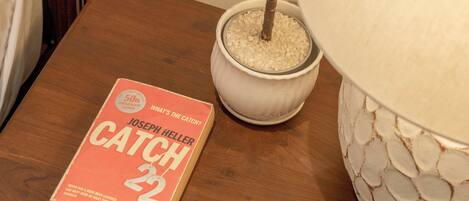 A book titled 'CATCH 22' by Joseph Heller on a wooden table, a potted plant, and a decorative lamp.