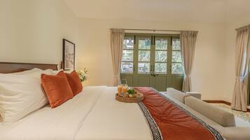 A neatly made bed with pillows, a tray with drinks and a plant, and a view of a green door and windows.