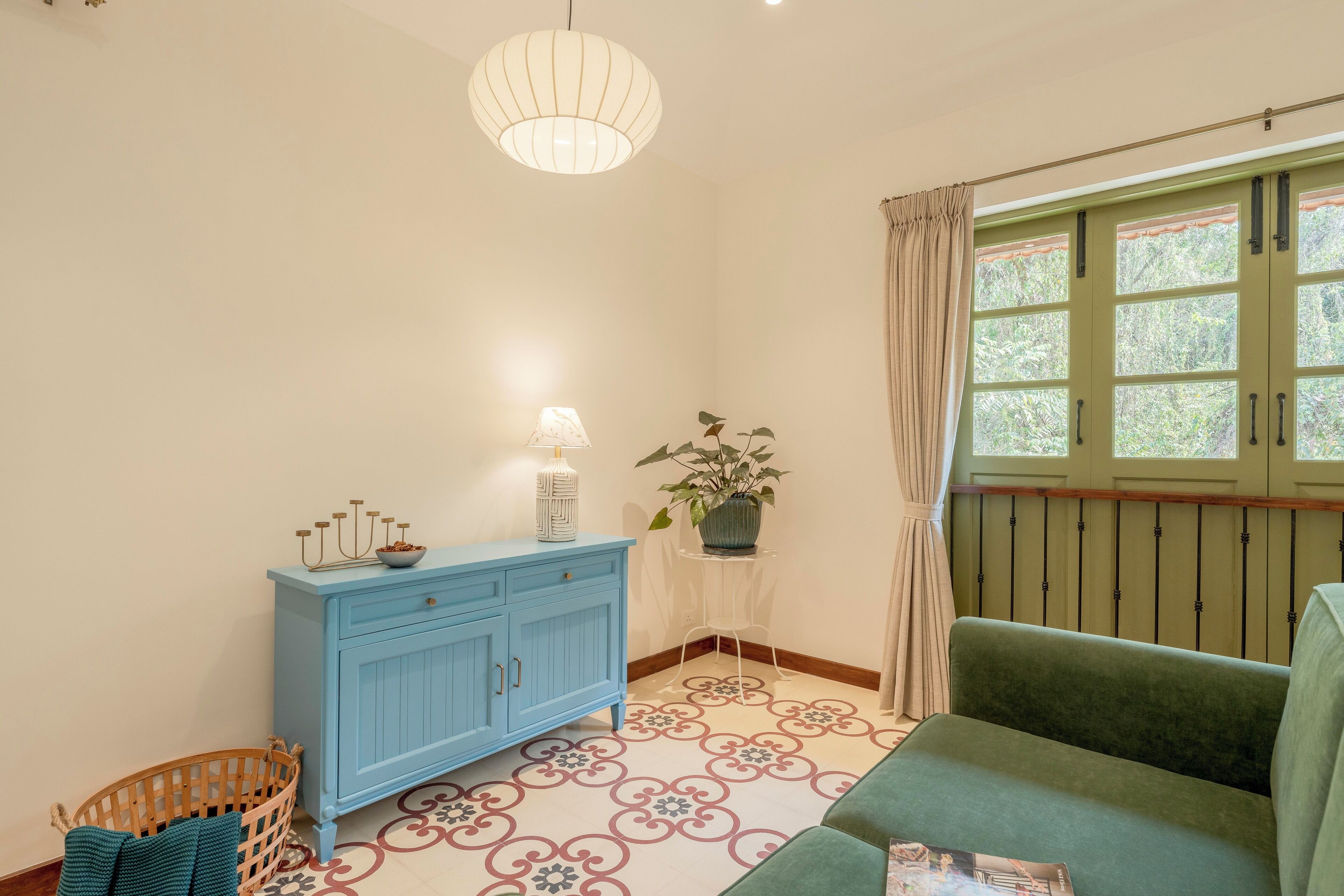 A room with a blue cabinet, a green sofa, a patterned floor, a hanging light fixture, and a window with curtains.