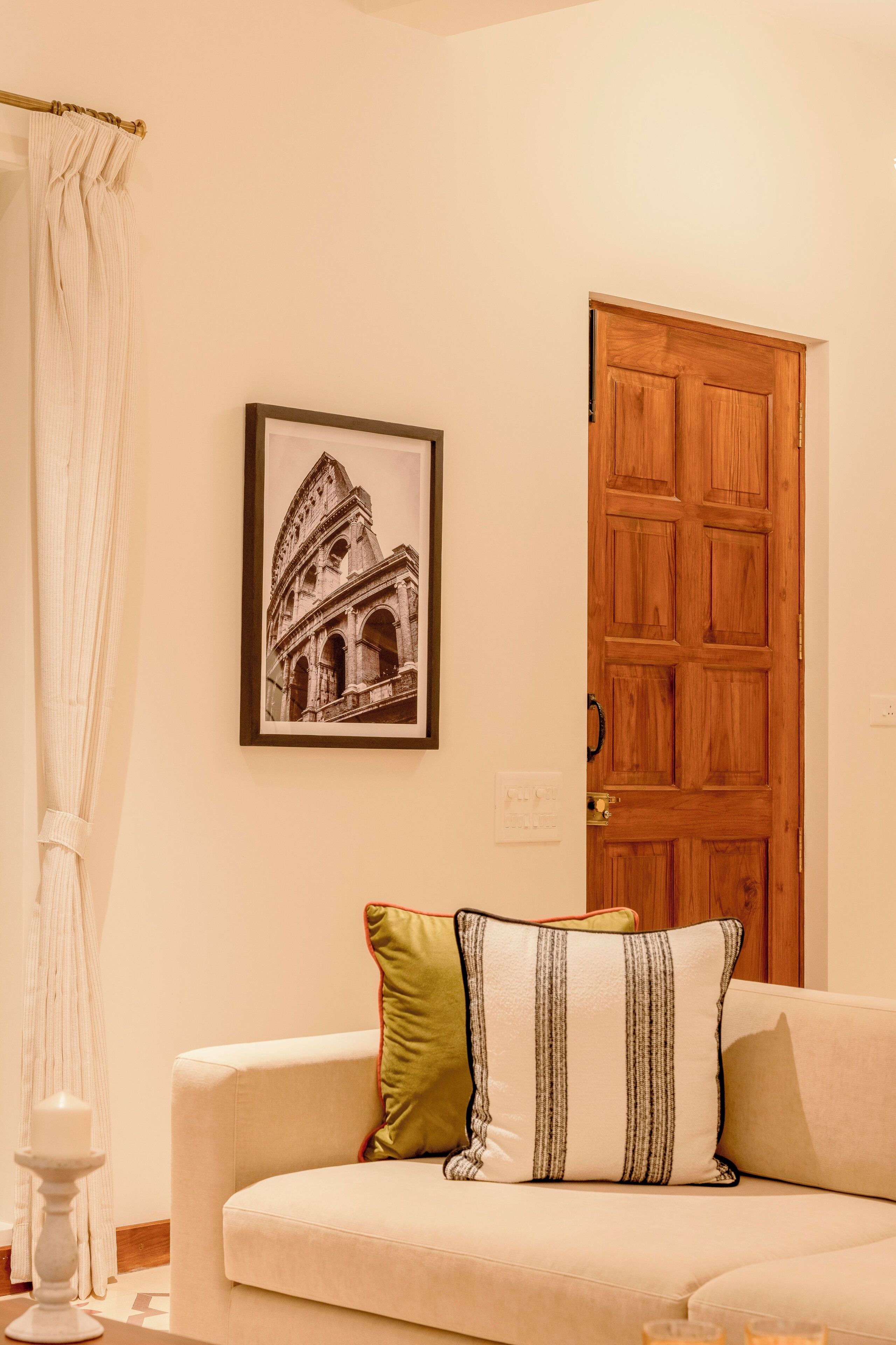Una habitación con un cuadro enmarco de un edificio histórico, una puerta de madera y un sofá beige con almohadones a rayas.