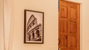 Una habitación con un cuadro enmarco de un edificio histórico, una puerta de madera y un sofá beige con almohadones a rayas.