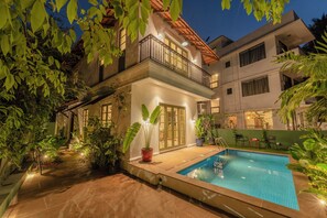 Une maison à deux étages avec une piscine, entourée de plantes en pot et dotée d’un patio.