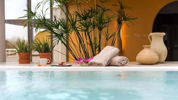 Zona junto a la piscina con vista despejada al agua, plantas en macetas, un florero y toallas.