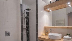 Un bagno moderno con il water bianco, una doccia con porta in vetro, un mobile bagno in legno con lavandino e uno specchio sopra.