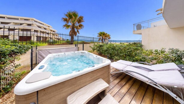 Ein Whirlpool auf einer Holzterrasse mit Blick auf ein Gebäude und Palmen.