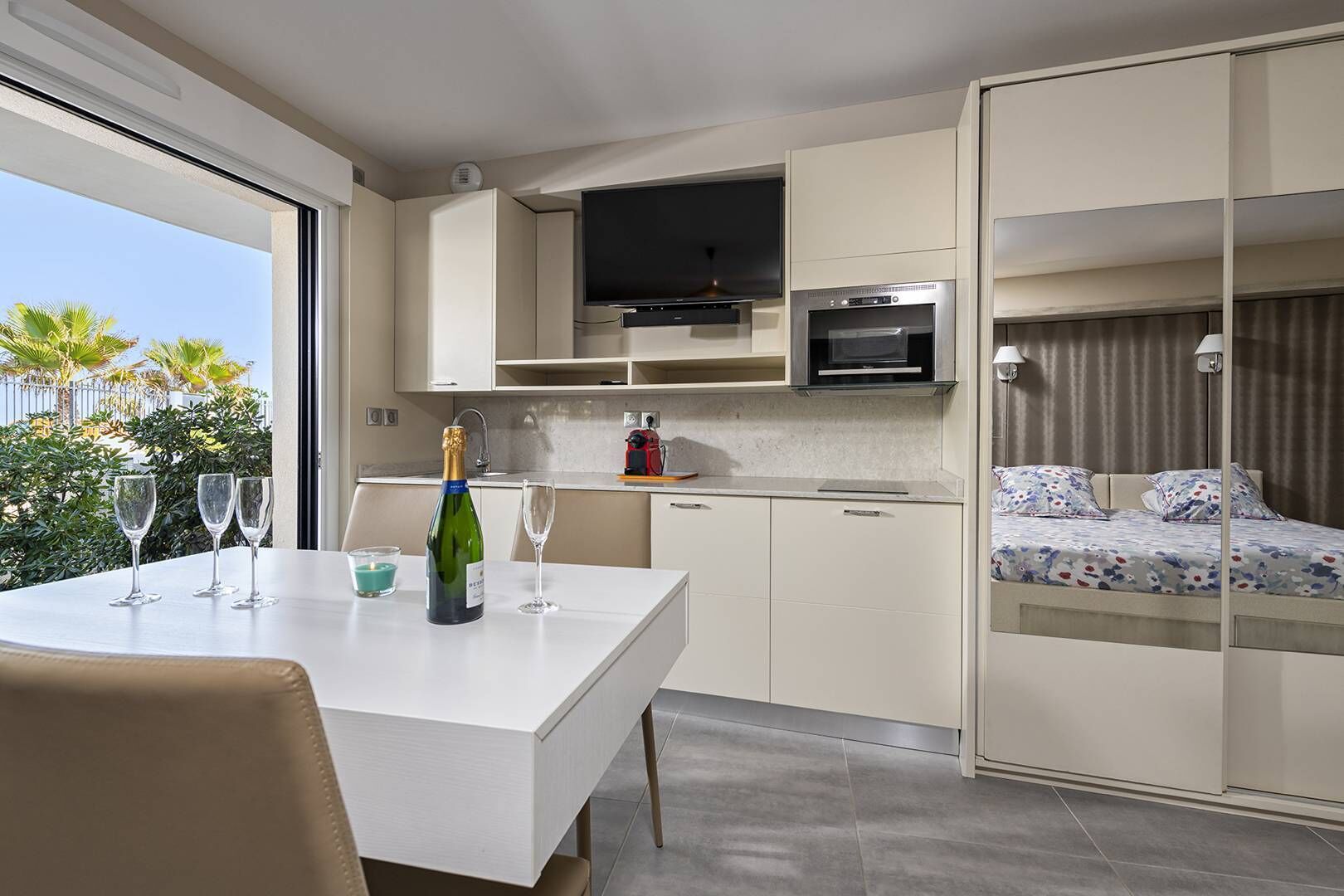 Cocina compacta con comedor, televisor y cama con colcha estampada.