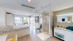 A modern bedroom with a bed, a glass shower enclosure, a vanity with a mirror, and a view of the outdoors. - NAUTILIA  103 - Premium Luxe - Jacuzzi - 2 people (AGDE)