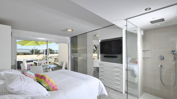A modern bedroom with a bed, a TV, a glass shower enclosure, and a balcony with outdoor furniture. - NAUTILIA  103 - Premium Luxe - Jacuzzi - 2 people (AGDE)
