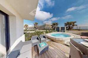 Un área de piscina en la azotea con un jacuzzi, mobiliario exterior y vistas a la playa y los edificios del hotel.