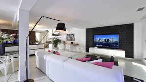 Una sala de estar moderna con un sofá blanco, un televisor de pantalla plana y una escalera que sube a un nivel superior.