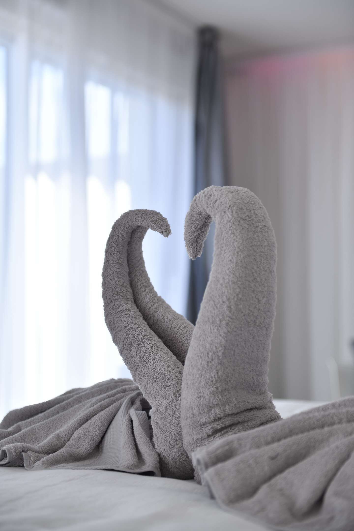 A bed with two towels arranged in a heart shape.