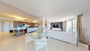 Ein moderner Wohnraum mit Essbereich, Küche und einem großen Fenster mit Vorhängen.