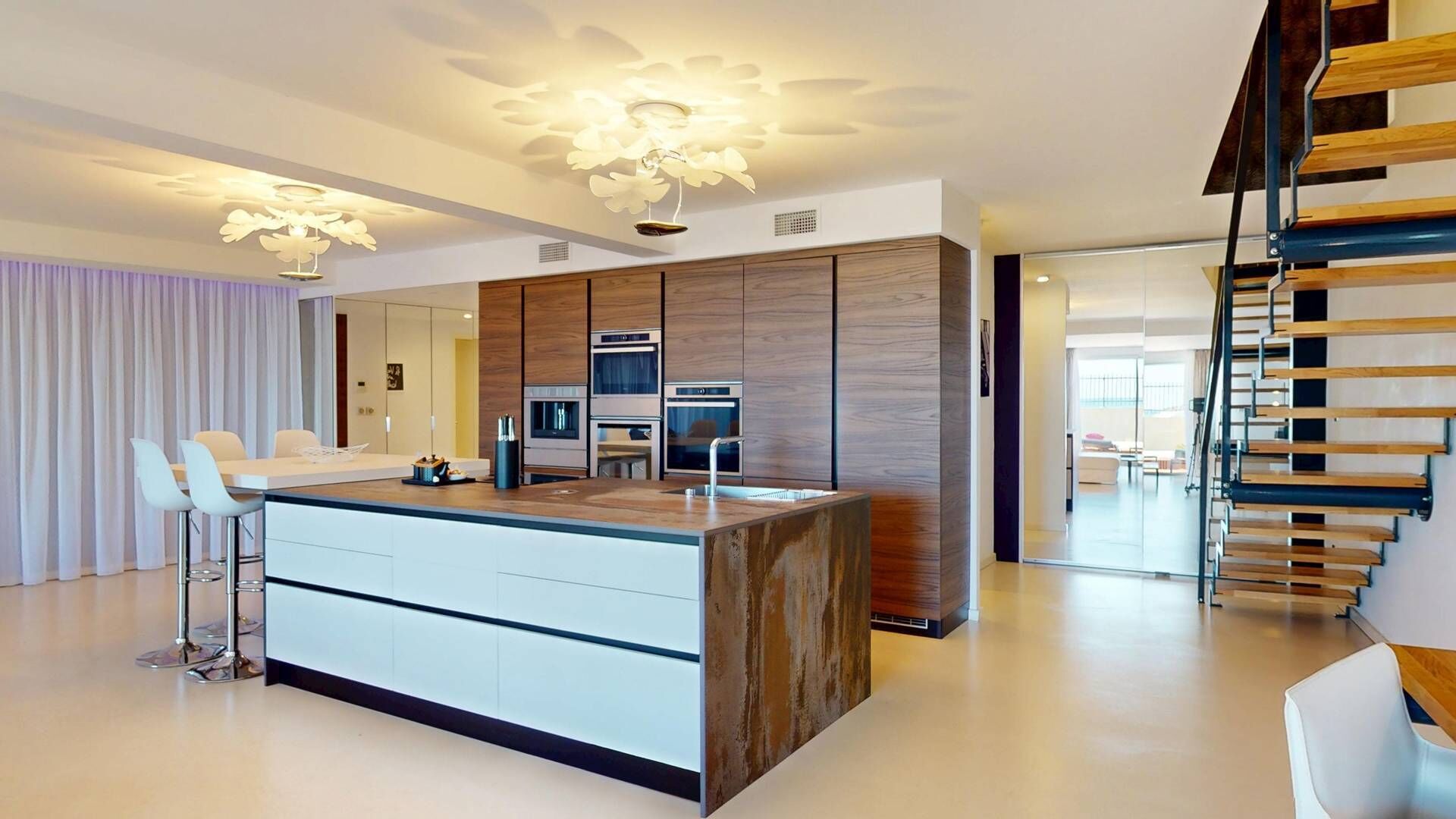A modern kitchen with a central island, built-in appliances, and a staircase.