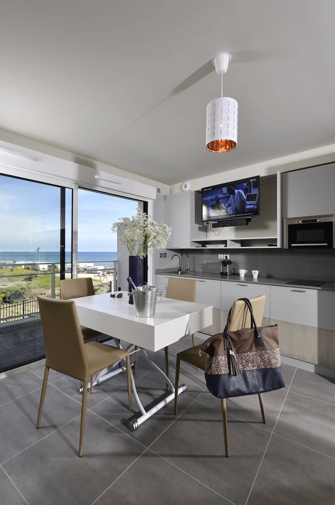 Una cocina moderna con televisor, mesa de comedor, sillas y vista al océano.
