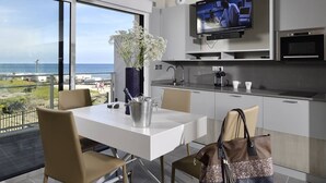 A modern kitchen with a TV, dining table, chairs, and a view of the ocean. - NAUTILIA  202 - Premium Luxe - Balcony - 2 people (AGDE)