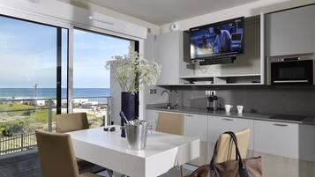 Una cocina moderna con televisor, mesa de comedor, sillas y vista al océano.