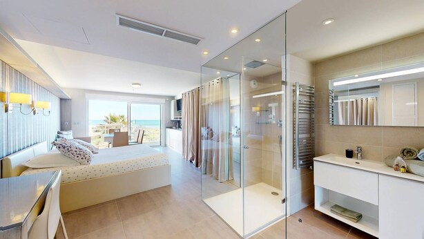 A modern bedroom with a bed, a glass shower enclosure, a bedside table, and a view of the beach. - NAUTILIA  202 - Premium Luxe - Balcony - 2 people (AGDE)