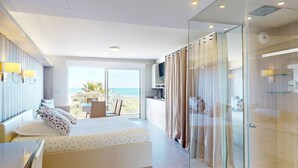 A modern hotel room with a bed, a desk, a balcony with a view of the sea, and a glass shower enclosure. - NAUTILIA  202 - Premium Luxe - Balcony - 2 people (AGDE)