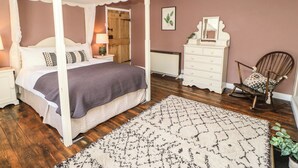 Un dormitorio con cama con dosel, cómoda, silla, radiador y espejo fijado a la pared.