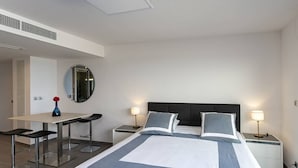 Ett modernt hotellrum med en stor säng, två sängbord, ett skrivbord med stolar och en spegel på väggen.