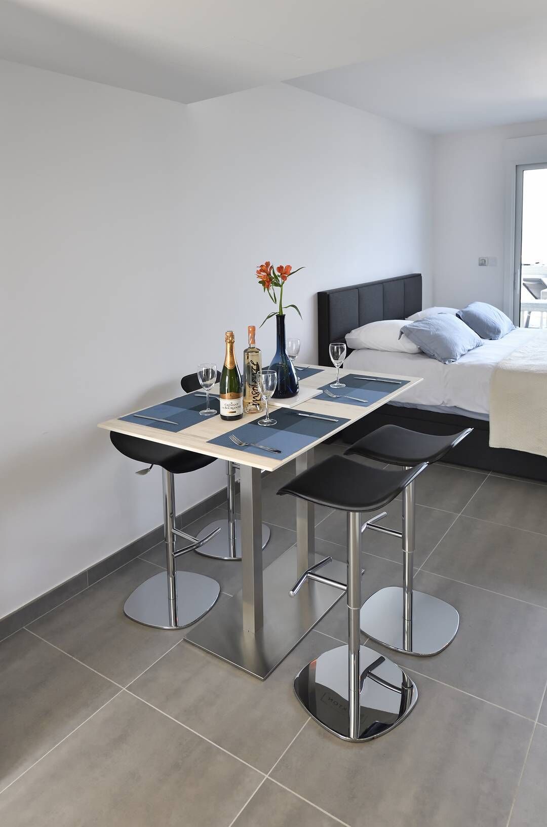Moderni hotellihuone, jossa on ruokailutila, johon kuuluu pöytä, tuolit ja maljakko, jossa on kukkia.