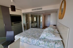 Ein modernes Schlafzimmer mit einem Bett, einem Glastisch, einem Fernseher und einem Kleiderschrank.