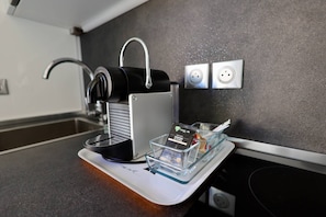 Eine Kaffeemaschine auf einer Arbeitsplatte, mit einem Glasbehälter, der eine Kapsel und einen kleinen Gegenstand enthält.