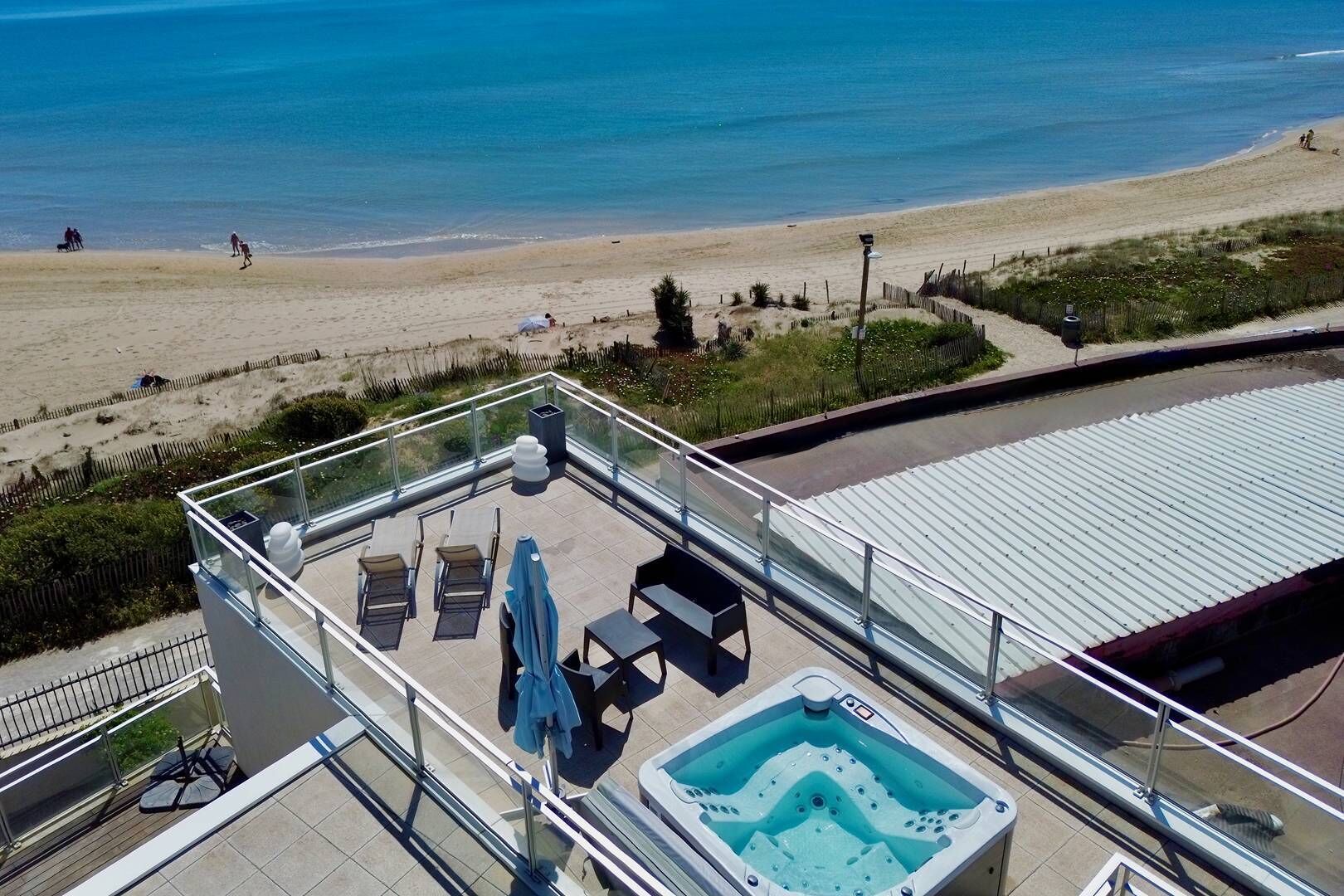 En takterrass med pool, solstolar och utsikt över stranden.