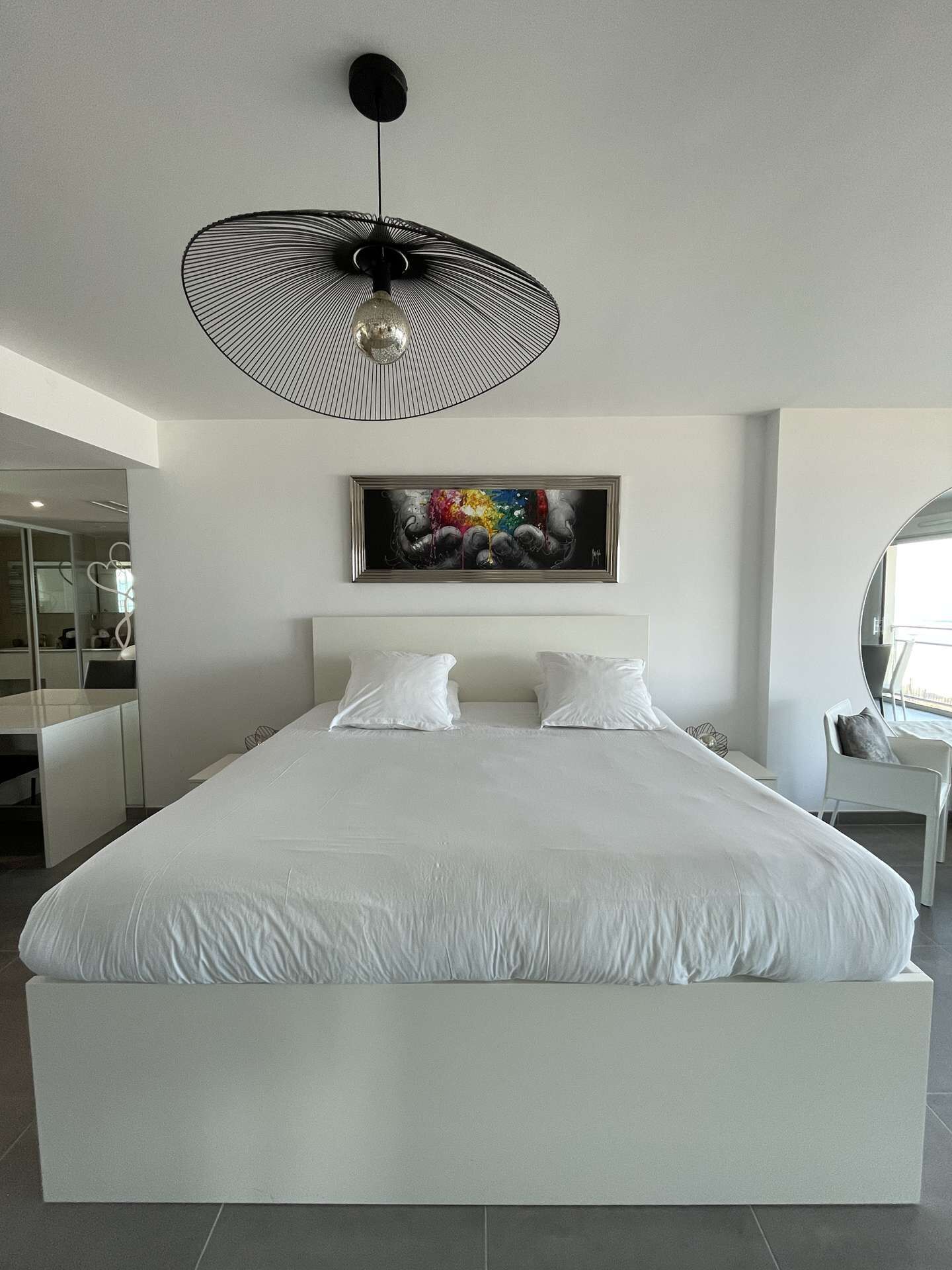 Ein modernes Schlafzimmer mit einem großen Bett, einem Deckenventilator, einem Wandbild und einem Spiegel.