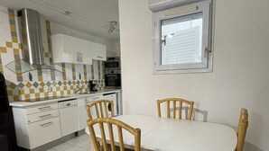 A kitchen with white cabinets, a dining table with four chairs, and a window above the table. - BUBBLE Natura Beach - Apartement NB2 - Luxe - 6 people (AGDE)