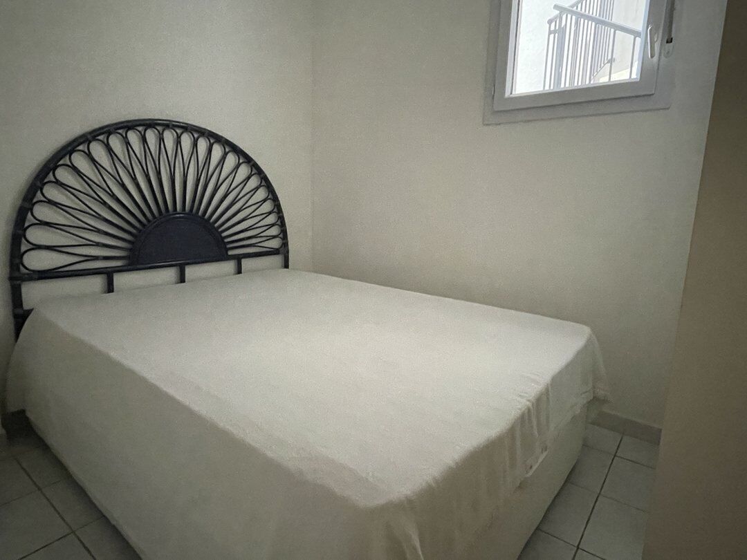 Una cama con cabecera de metal, una pared lisa y una ventana con vista a un balcón.