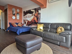 Ein Wohnzimmer mit einer Couch, einem Hocker und einem Bett mit blauer Bettwäsche.