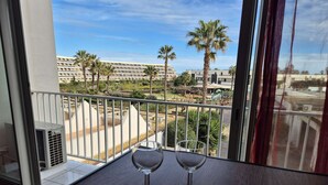 En balkong med utsikt över ett hotellkomplex, ett bord med vinglas och bestick samt ett fönster med gardiner.