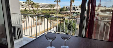 A balcony with a view of a hotel complex, a table with wine glasses and cutlery, and a window with curtains.