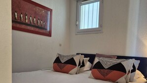 A bedroom with a bed, pillows, a window, and a wall-mounted air conditioner. - Apartment Natura Beach 203 with parking space - 4 people (AGDE)