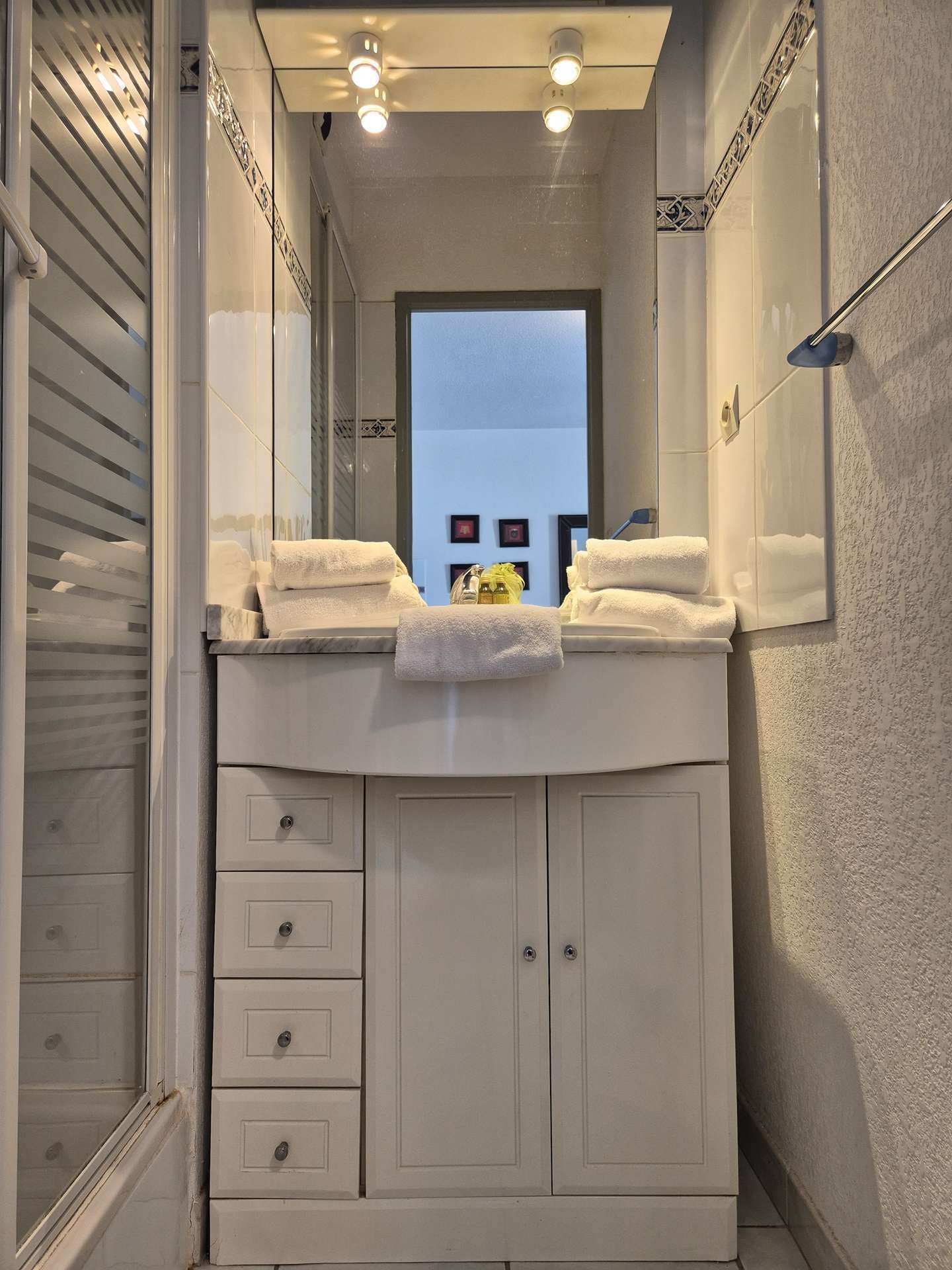Een smalle badkamer met een spiegel, een wastafel en een handdoekhouder.