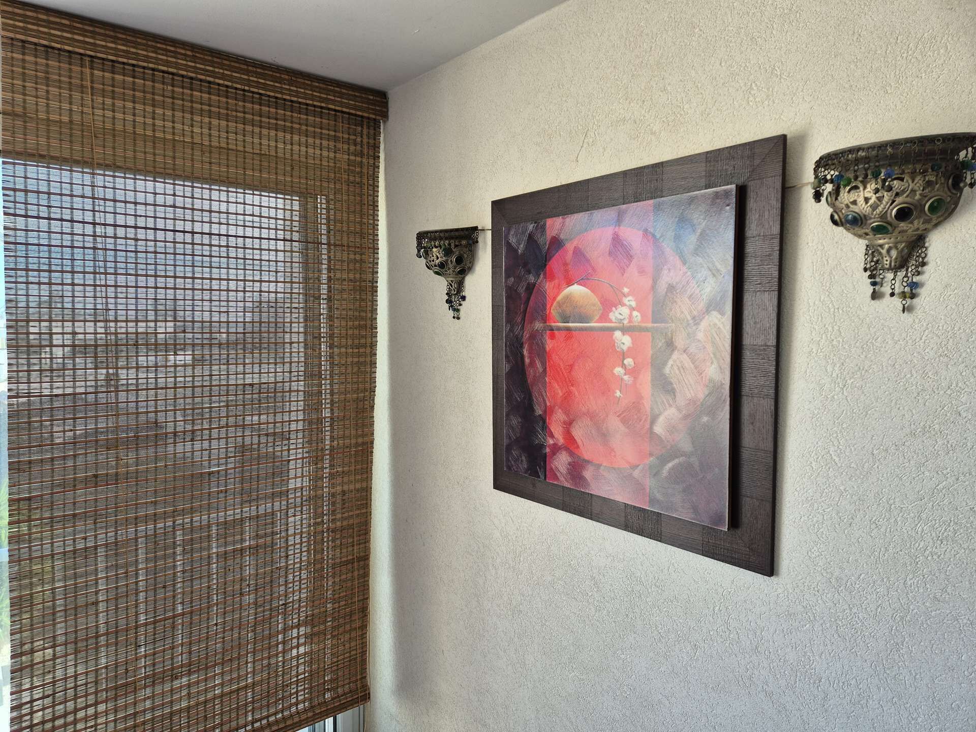 A room with a wall-mounted painting, a textured wall, and a window with a woven blind.